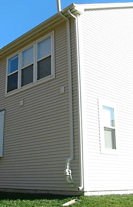 Radon mitigation fan mounted on a vent pipe running up the exterior wall of a house